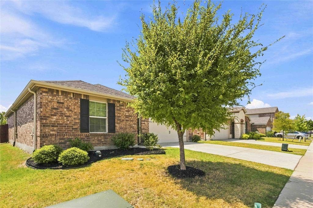 Single-story brick exterior featuring dark shutter accents, concrete driveway, and landscaped front garden