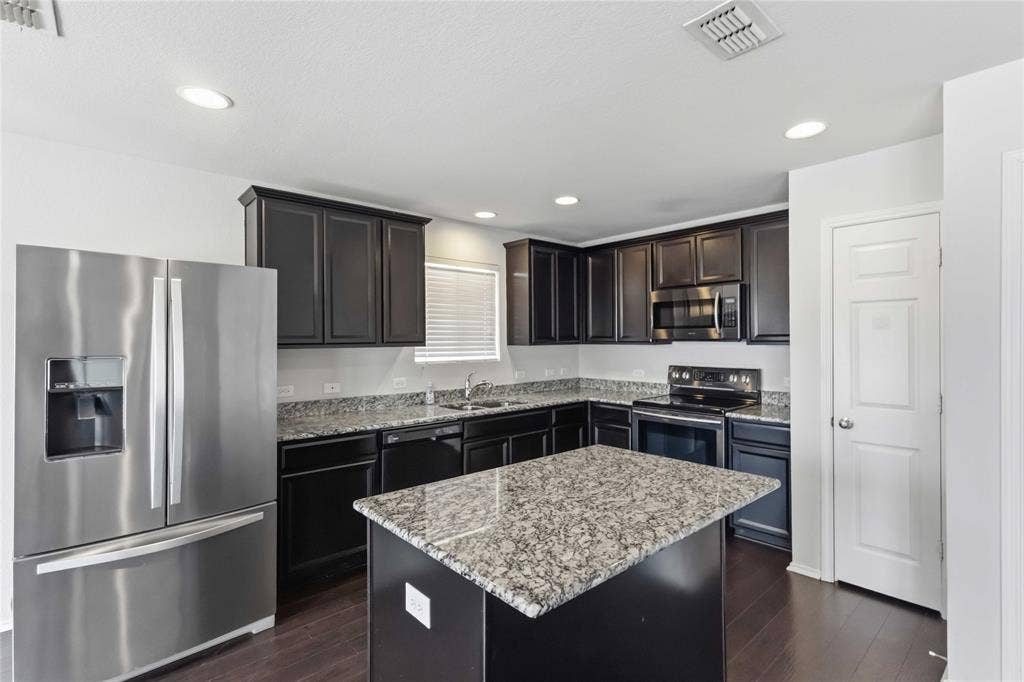 Kitchen featuring dark wood cabinetry, stone countertops, stainless steel appliances, a center island, and wood-finish flooring