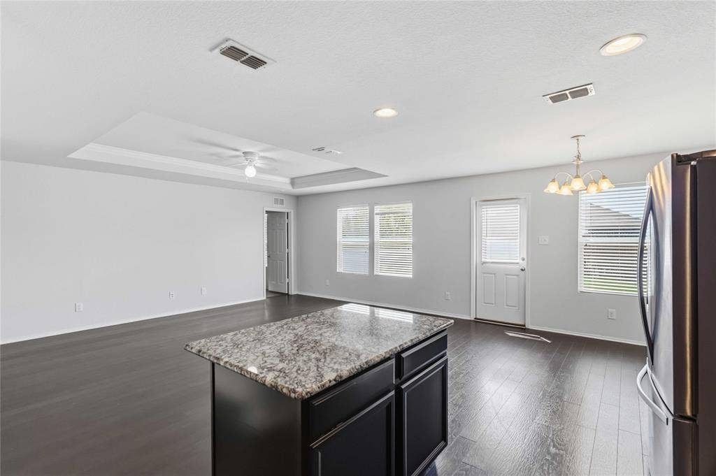 Open-concept living space featuring wood-finish flooring, a tray ceiling with a ceiling fan, a kitchen island with a stone-finish countertop, and recessed lighting