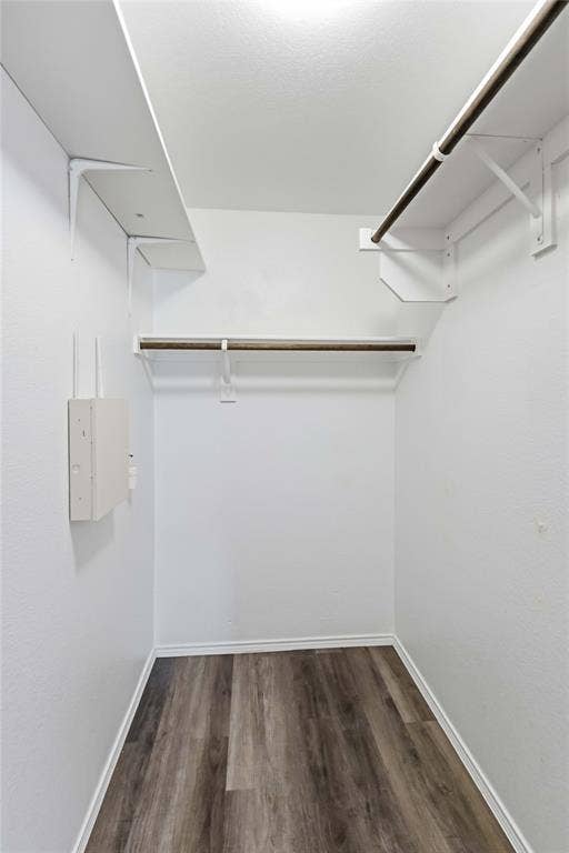 Walk-in closet featuring wood-finish flooring and tiered white shelving with integrated clothing rods