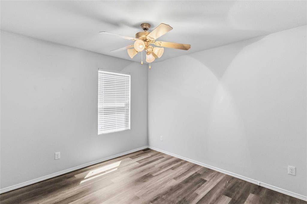 Wood-finish flooring, neutral walls, and a ceiling fan with integrated multi-bulb light fixture, featuring a window with horizontal blinds