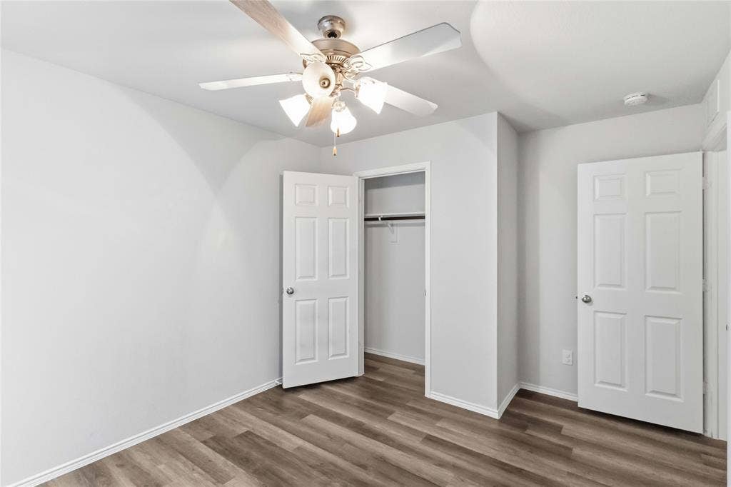 Room featuring wood-finish flooring, a multi-blade ceiling fan with integrated lighting, and six-panel interior doors