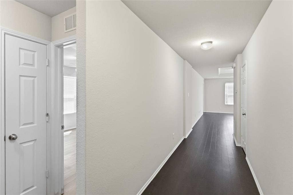 Interior hallway featuring dark wood-finish flooring, neutral wall tones, multi-panel doors, and a ceiling-mounted flush lighting fixture