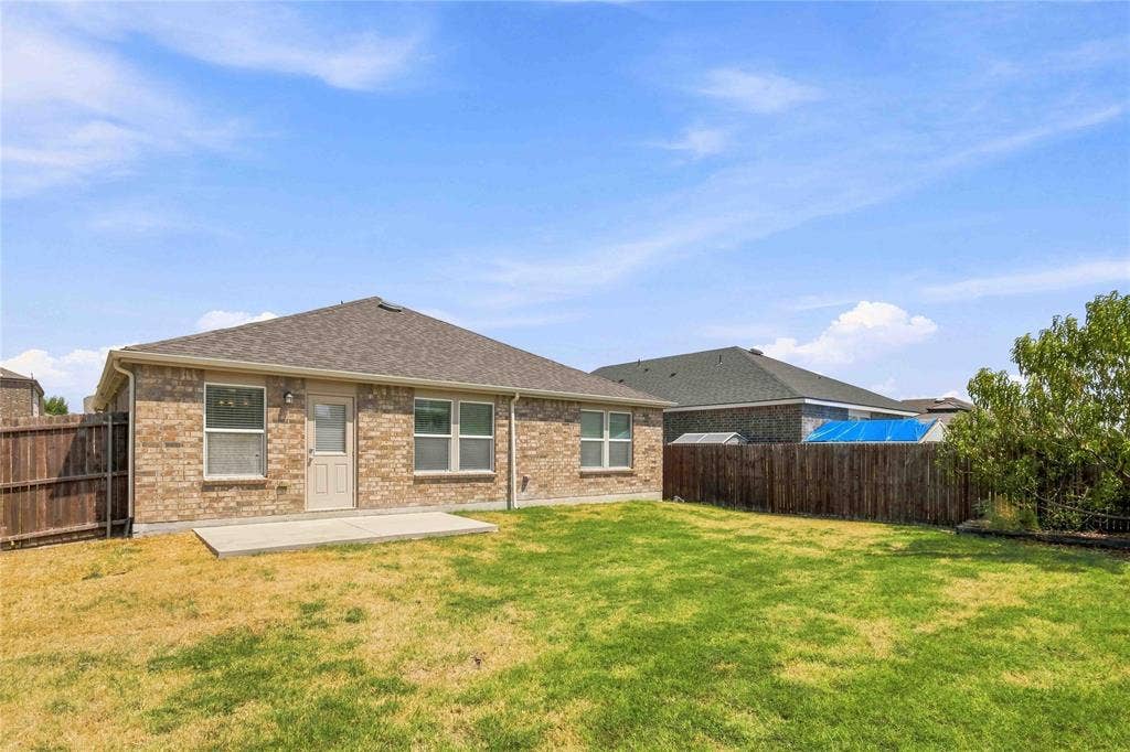 Brick exterior with a hipped roofline, concrete patio, and enclosed wood fencing