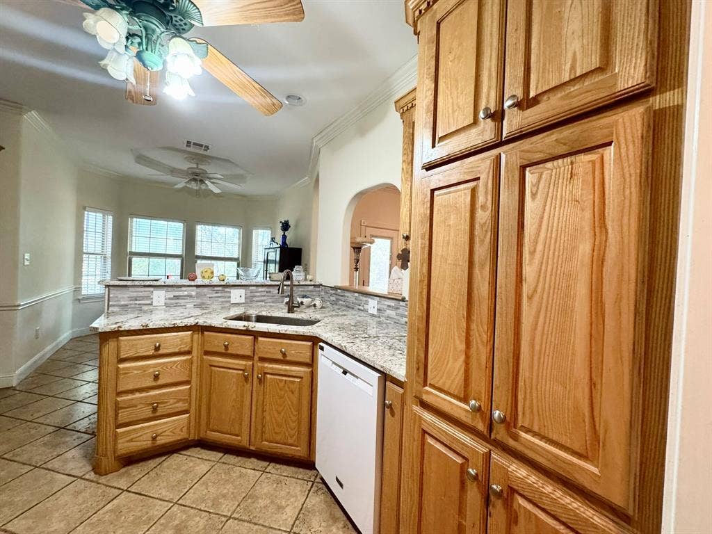 3700 NE County Road 0095, Corsicana, TX 75109 Kitchen featuring wood cabinetry, stone countertops, a mosaic tile backsplash, a stainless steel undermount sink with a pull-down faucet, and tiled flooring