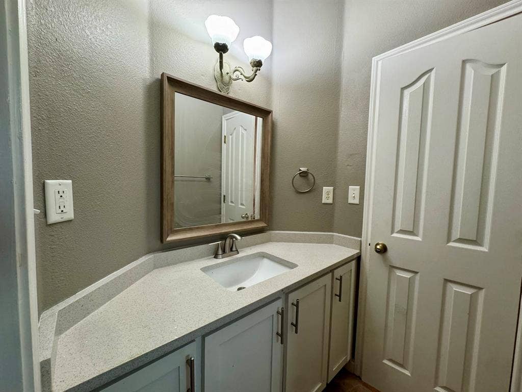 3700 NE County Road 0095, Corsicana, TX 75109 Vanity featuring a light-toned countertop, undermount sink, shaker-style cabinetry, framed wall mirror, and dual-light wall-mounted fixture