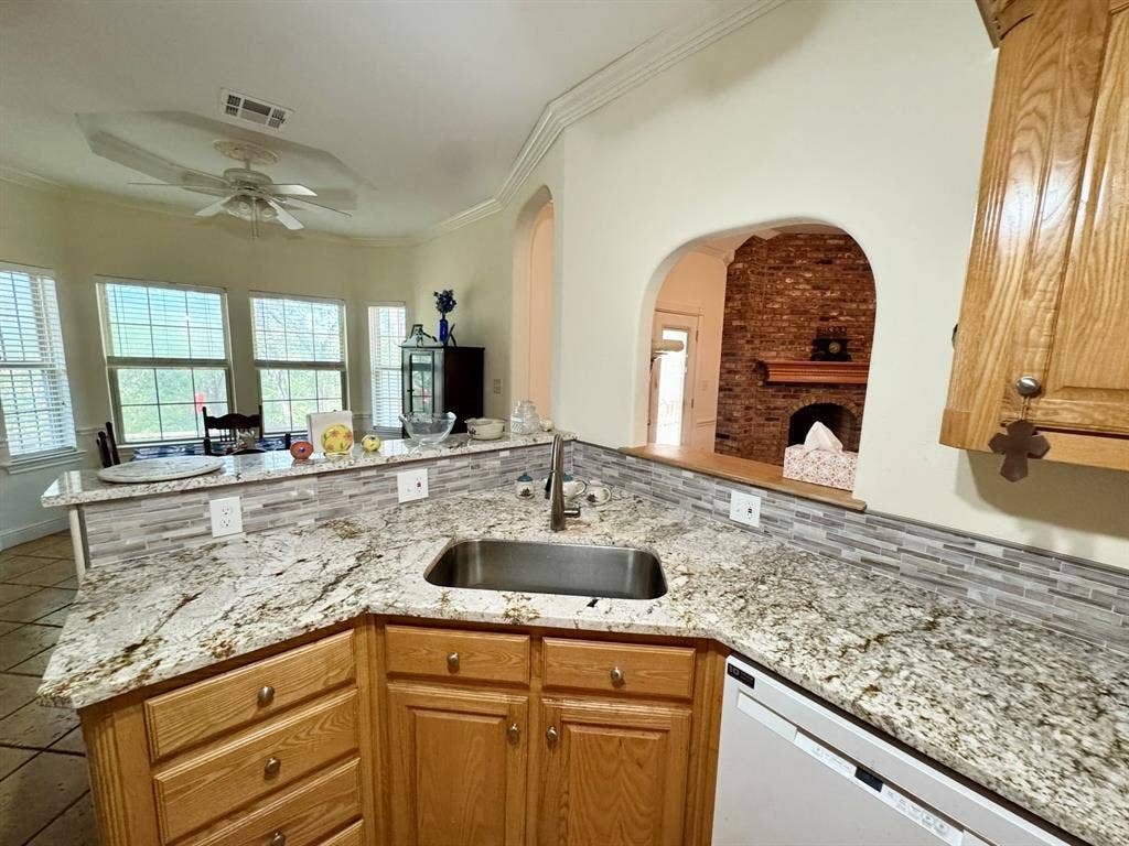 3700 NE County Road 0095, Corsicana, TX 75109 Kitchen featuring stone-finish countertops, mosaic tile backsplash, wood-finish cabinetry, stainless steel sink, and arched wall detailing