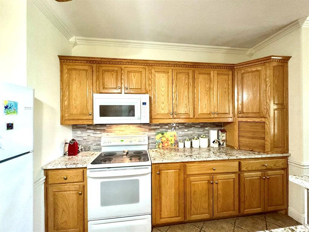 3700 NE County Road 0095, Corsicana, TX 75109 Kitchen featuring wood cabinetry, stone-finish countertops, mosaic tile backsplash, crown molding, and built-in appliance integration