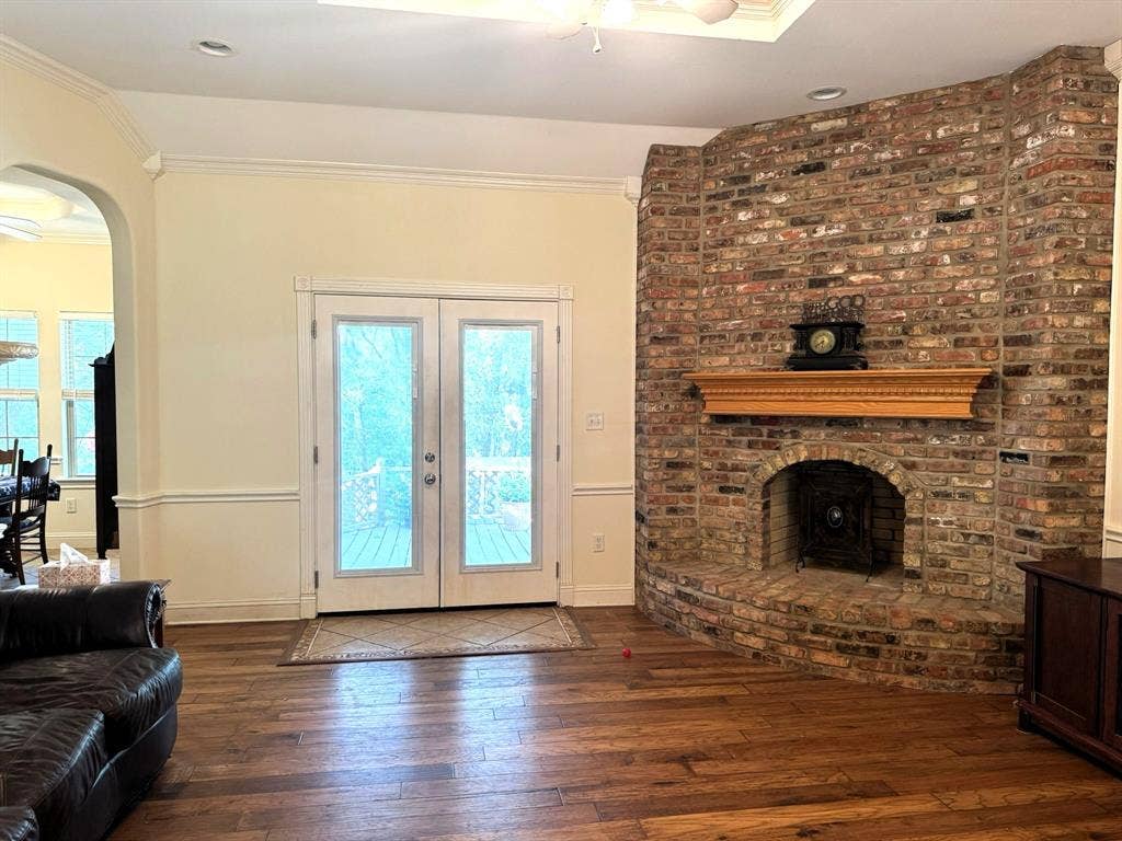 3700 NE County Road 0095, Corsicana, TX 75109 Floor-to-ceiling brick fireplace with an arched firebox and decorative wood mantel, wood-finish flooring, double glass-paneled doors, tray ceiling with recessed lighting, and crown molding