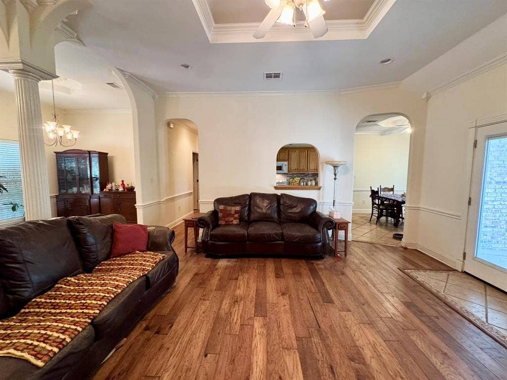 3700 NE County Road 0095, Corsicana, TX 75109 Open-concept interior featuring wood-finish flooring, tray ceilings with crown molding, decorative columns, and arched wall openings