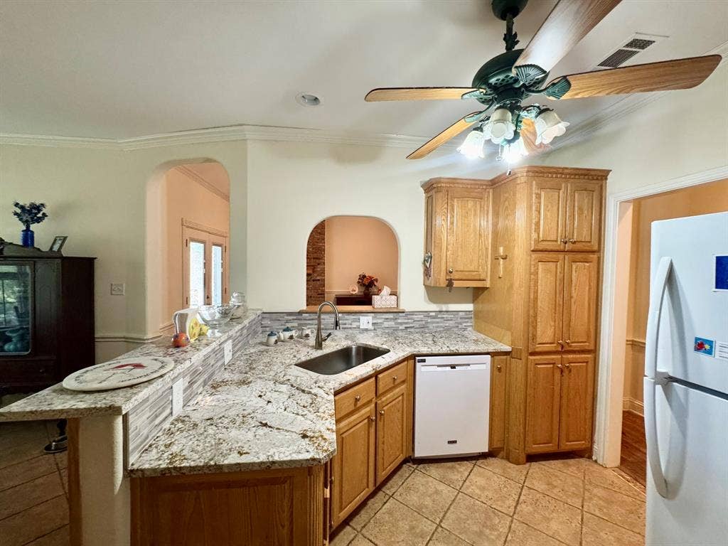 3700 NE County Road 0095, Corsicana, TX 75109 Kitchen featuring stone-finish countertops, tile backsplash, built-in light-tone wood cabinetry, tile flooring, and a ceiling-mounted fan with integrated lighting