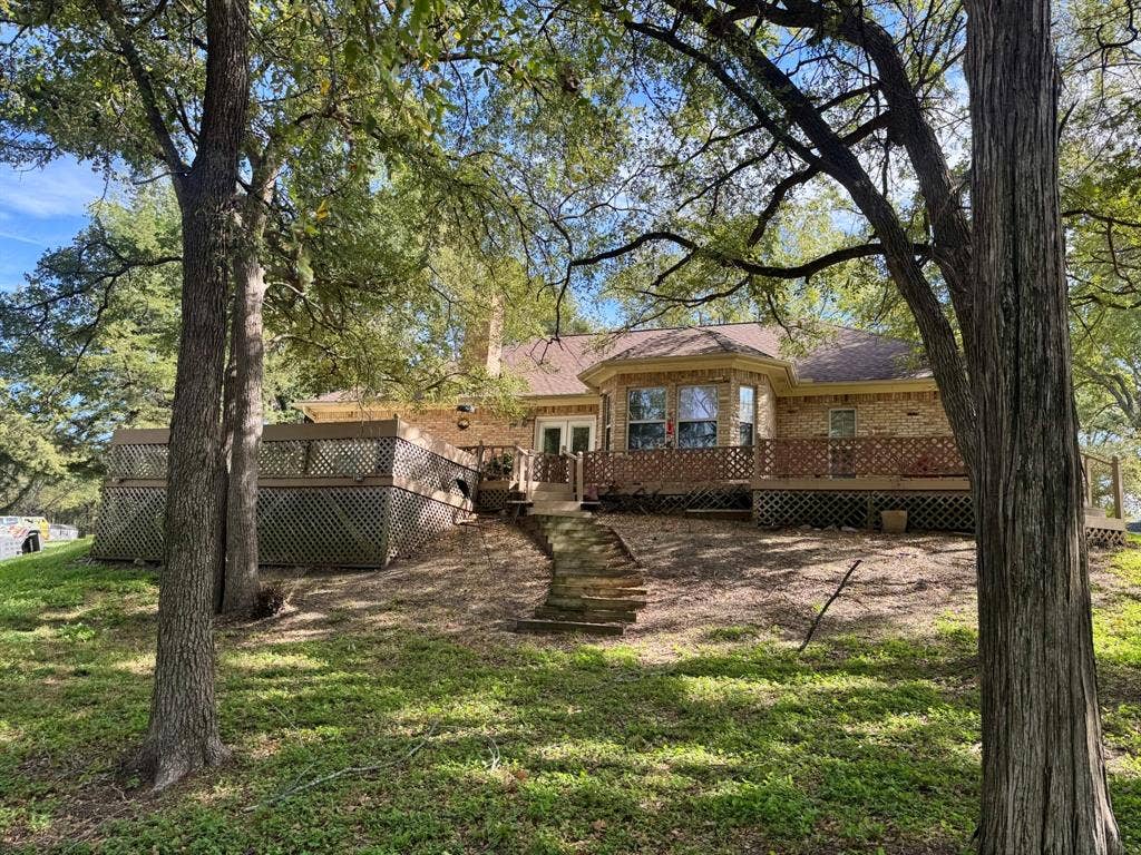 3700 NE County Road 0095, Corsicana, TX 75109 Brick exterior featuring a multi-level wood deck with lattice skirting, stone slab steps, and mature trees