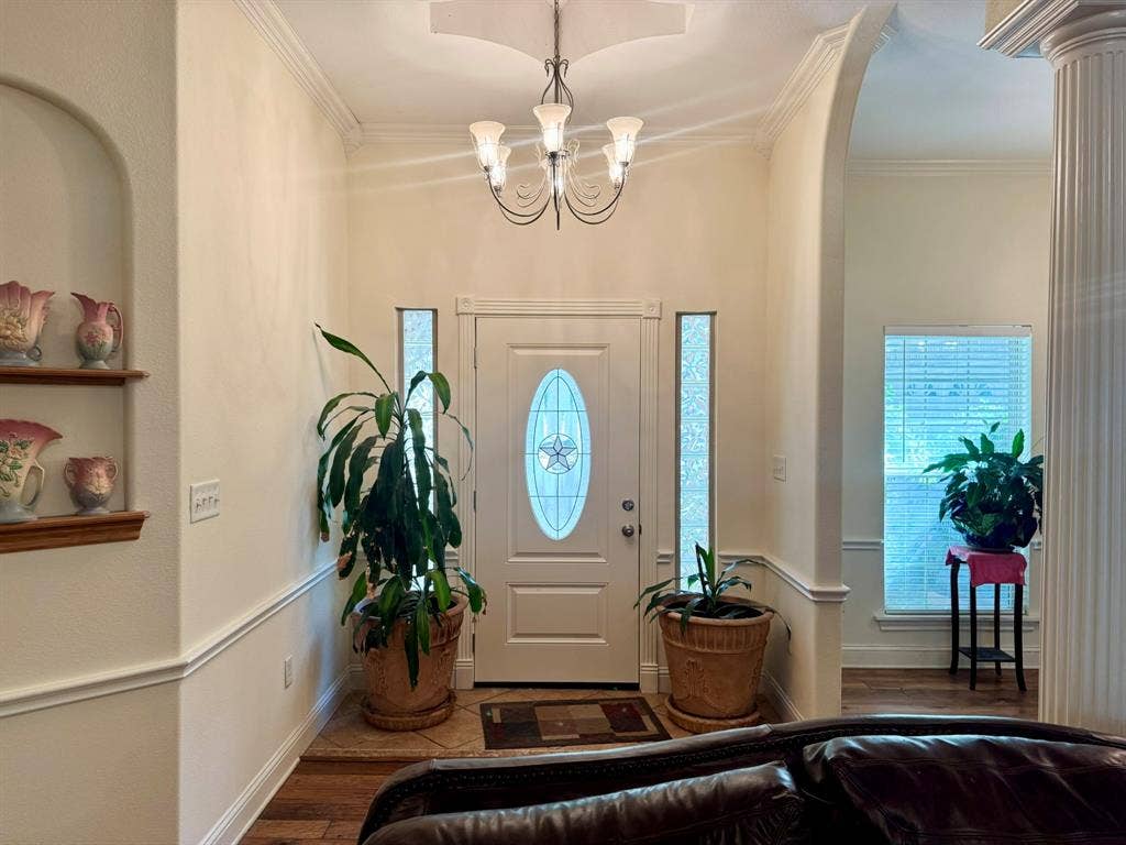 3700 NE County Road 0095, Corsicana, TX 75109 Entryway featuring arched architectural detailing, a central chandelier, decorative wall niche with built-in shelving, fluted column, and white door with oval glass insert flanked by narrow sidelights