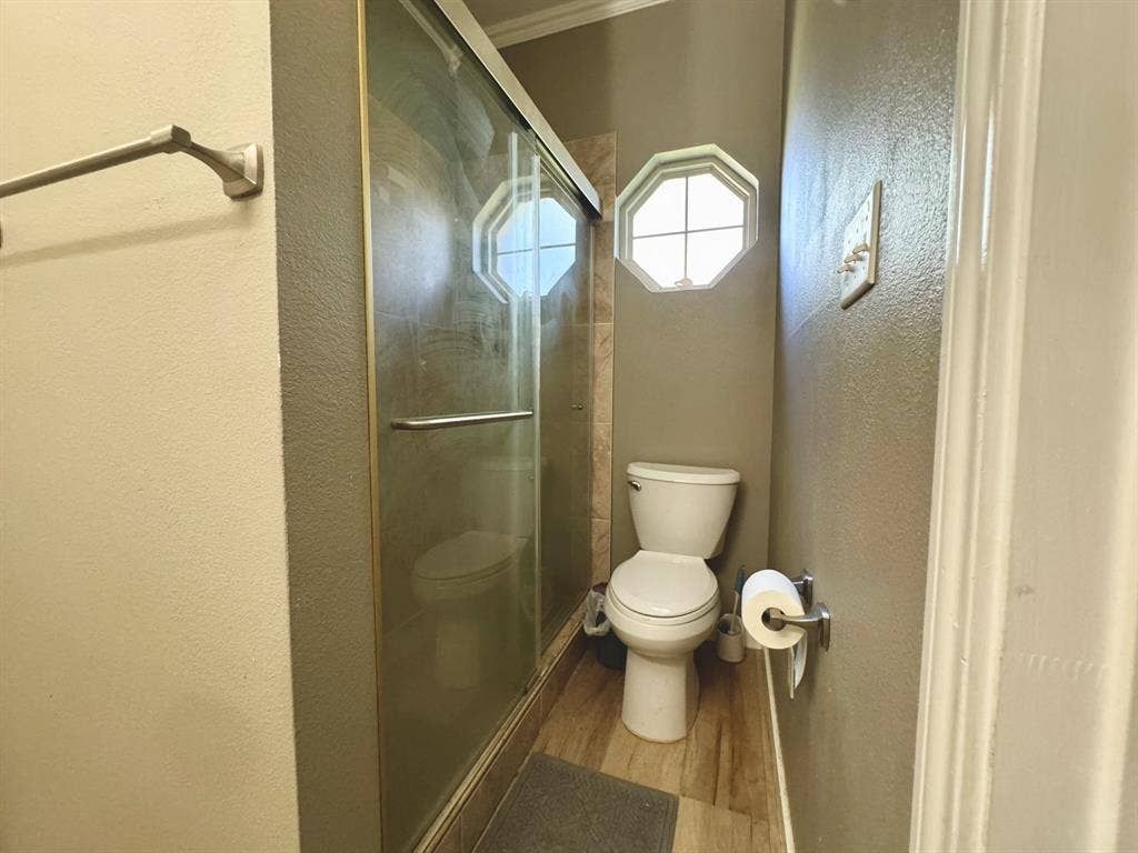 3700 NE County Road 0095, Corsicana, TX 75109 Shower enclosure with a sliding glass door, octagon-shaped window, and wood-finish flooring