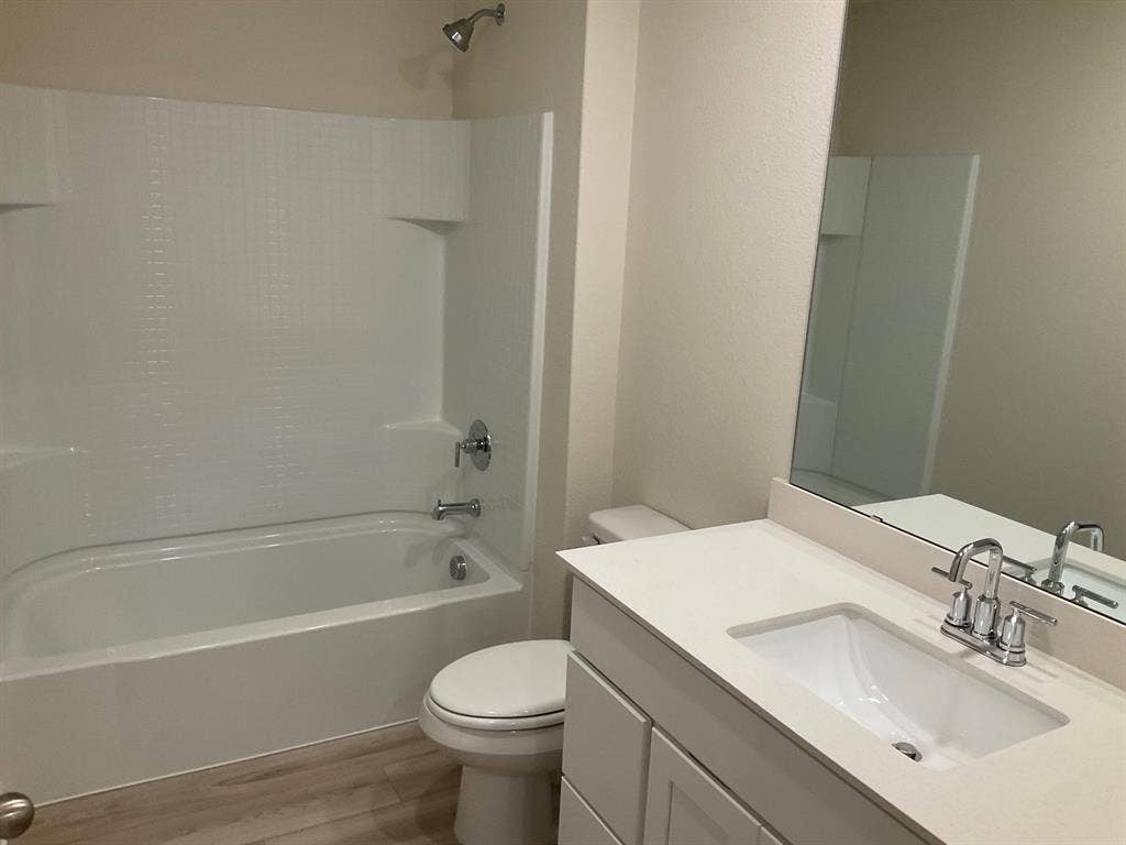 325 Stone Court, Princeton, TX 75407 Bathroom featuring a vanity with a white countertop and undermount sink, large wall-mounted mirror, wood-finish flooring, and a shower-tub combination with a white surround