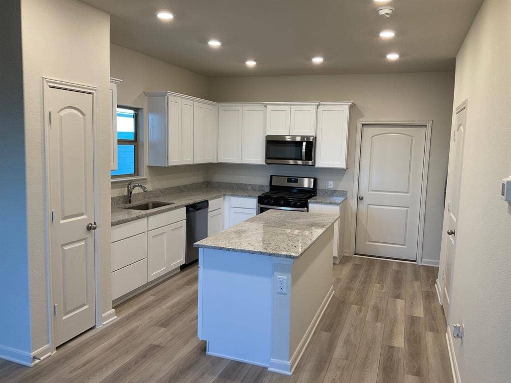 325 Stone Court, Princeton, TX 75407 Kitchen featuring white shaker-style cabinetry, stone-surface countertops, central island, stainless steel appliances, and wood-finish flooring