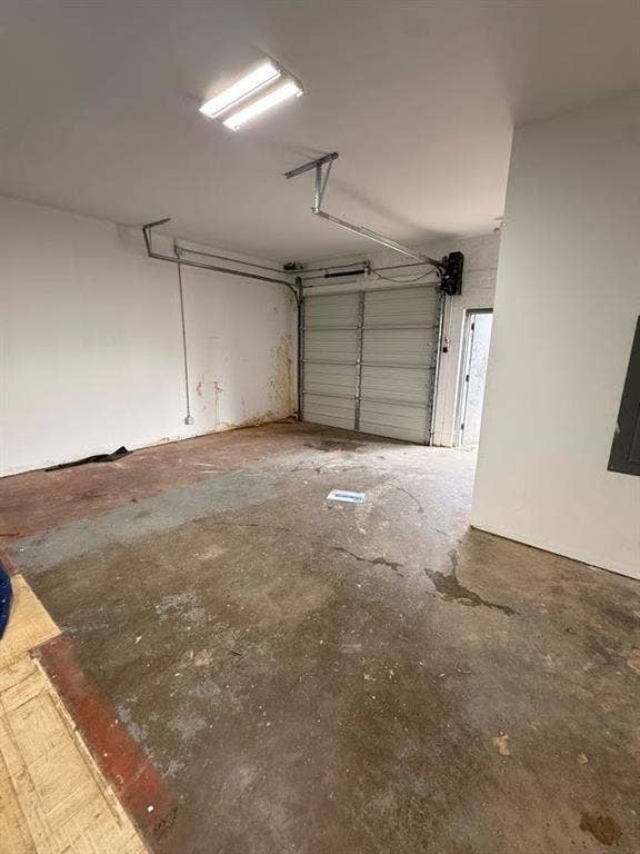 220 N Market Street, Shreveport, LA 71107 Enclosed garage featuring a metal sectional door, concrete flooring, overhead fluorescent lighting, and a pedestrian access door