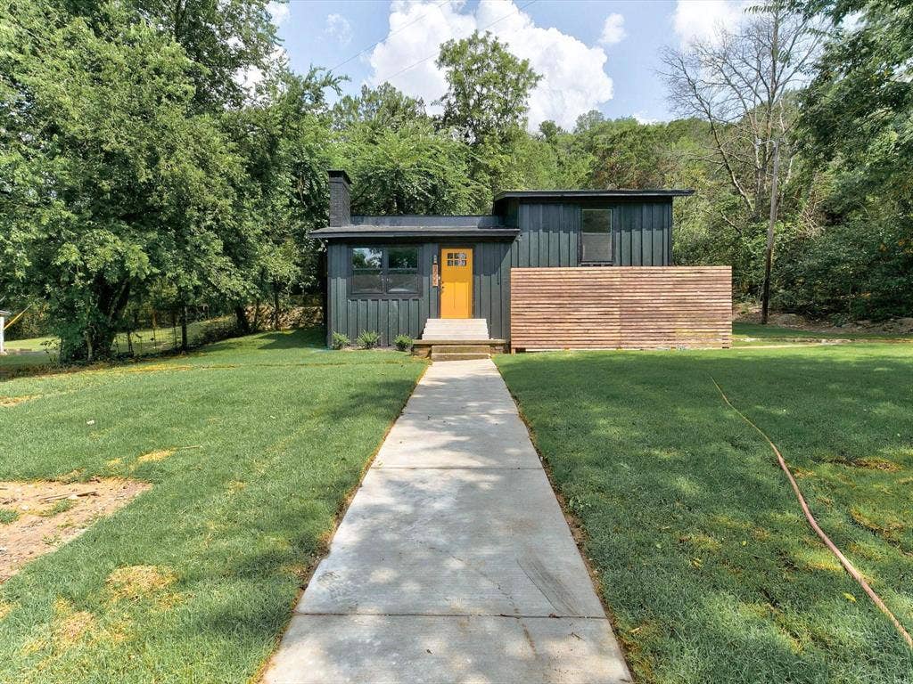 Modern exterior featuring vertical metal siding, horizontal wood-slat privacy screening, a prominent chimney stack, and a concrete walkway
