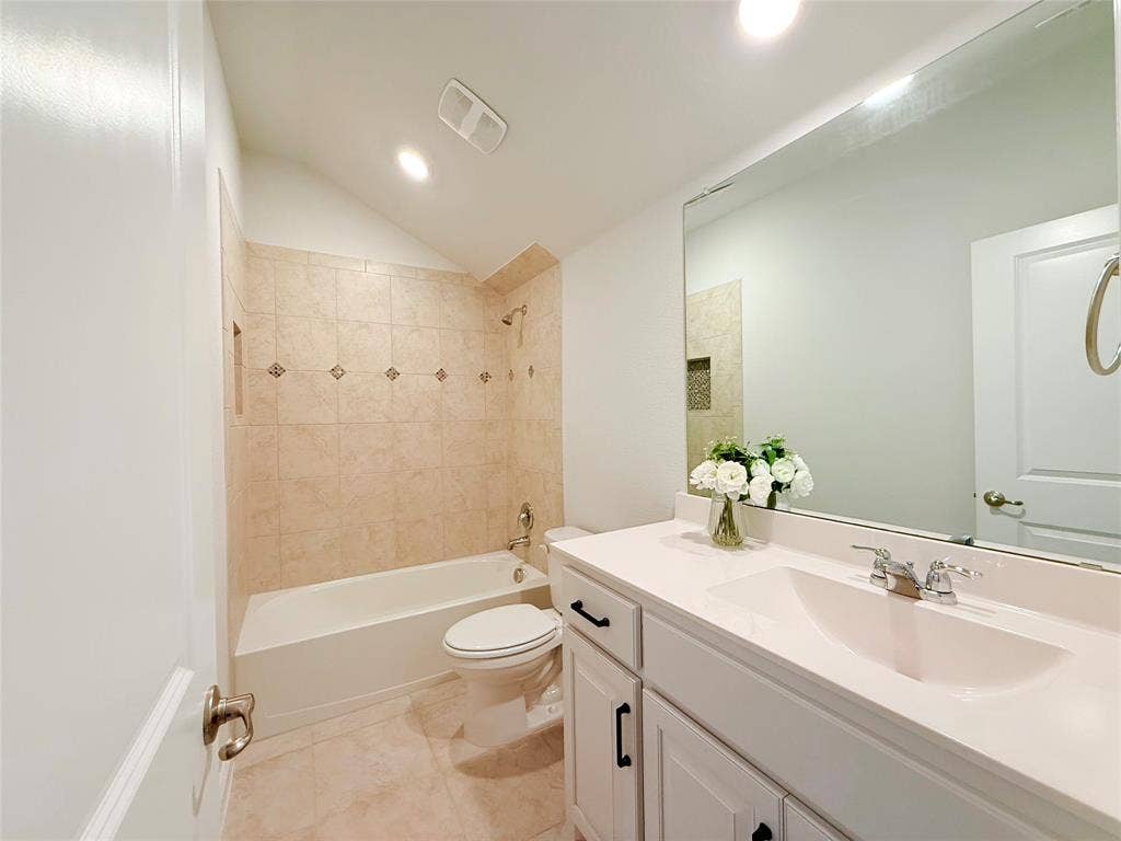 Bathroom featuring a vanity with a white countertop and rectangular undermount sink, white cabinetry with matte black hardware, a large wall-mounted mirror, and a tub-shower combination with tile surround and inset niche