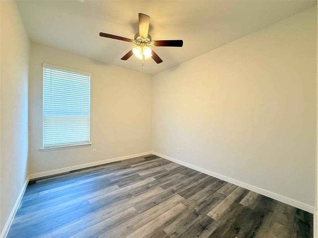 Room featuring wood-finish flooring, a neutral color palette, and an attached multi-blade ceiling fan with integrated lighting