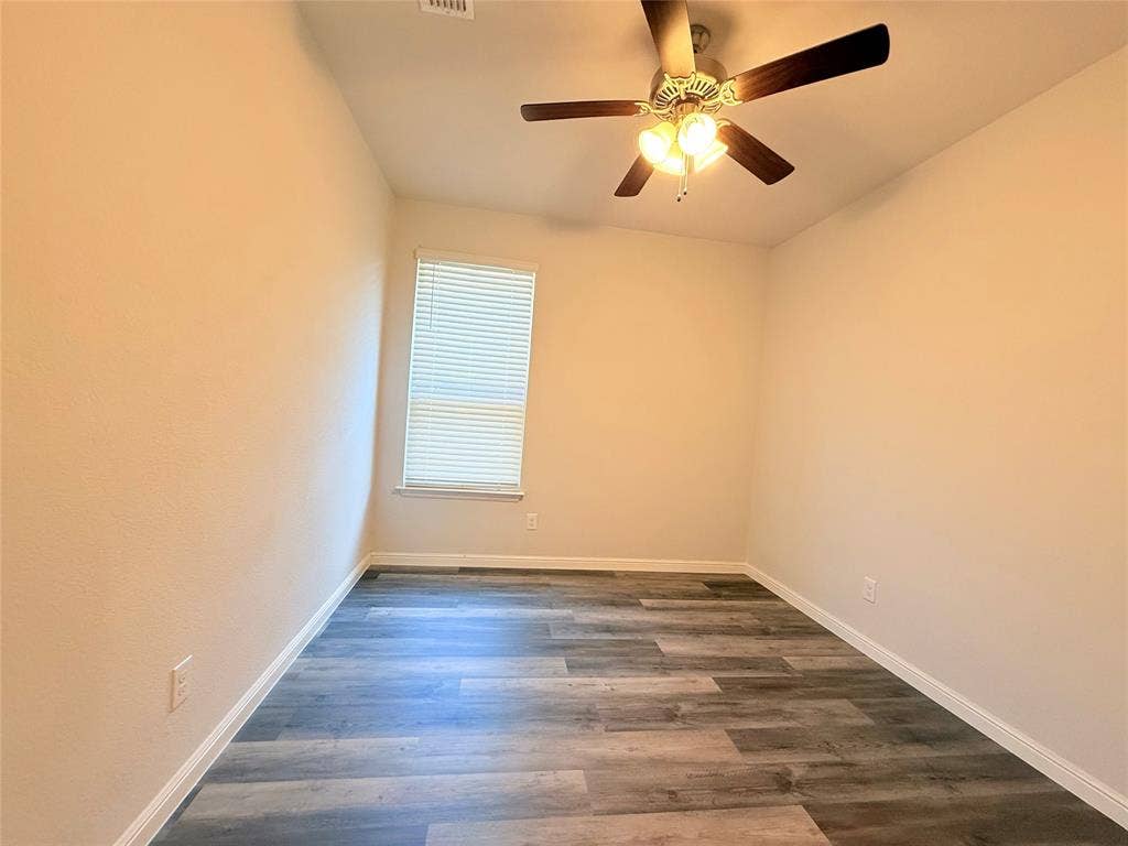 Room featuring wood-finish flooring, a neutral color palette, a single-window configuration with integrated blinds, and a multi-blade ceiling fan with light fixture