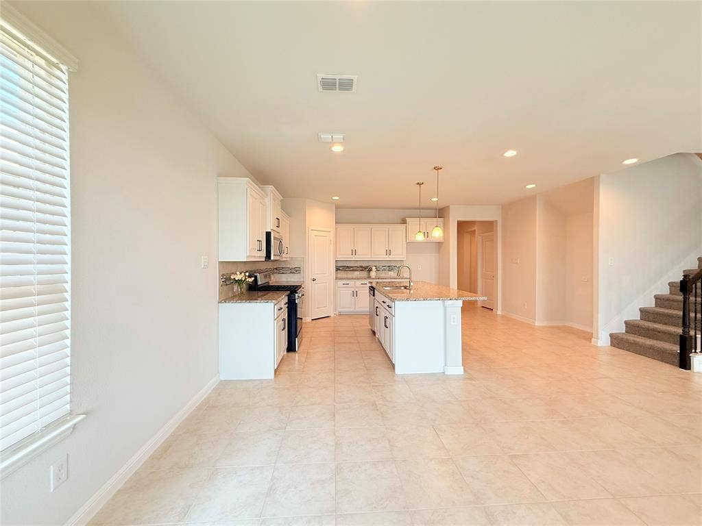 Kitchen featuring white cabinetry, stone-surface countertops, central island, tile flooring, and pendant lighting