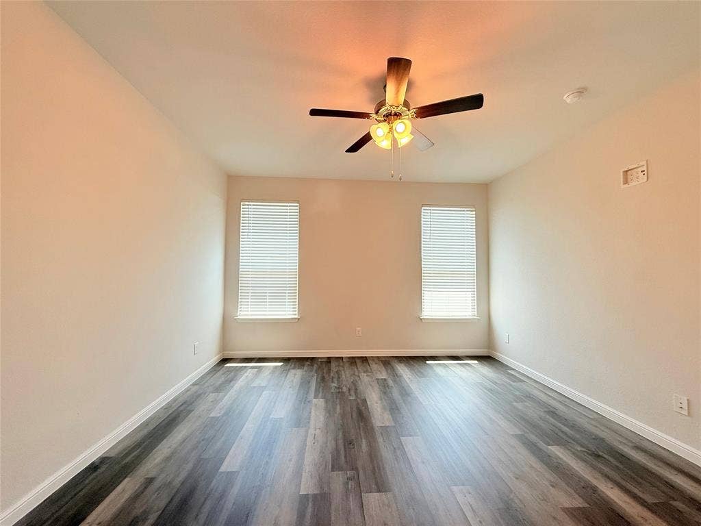 Neutral-toned interior space featuring wood-finish flooring, dual windows with integrated blinds, and a ceiling fan with multi-bulb light fixture