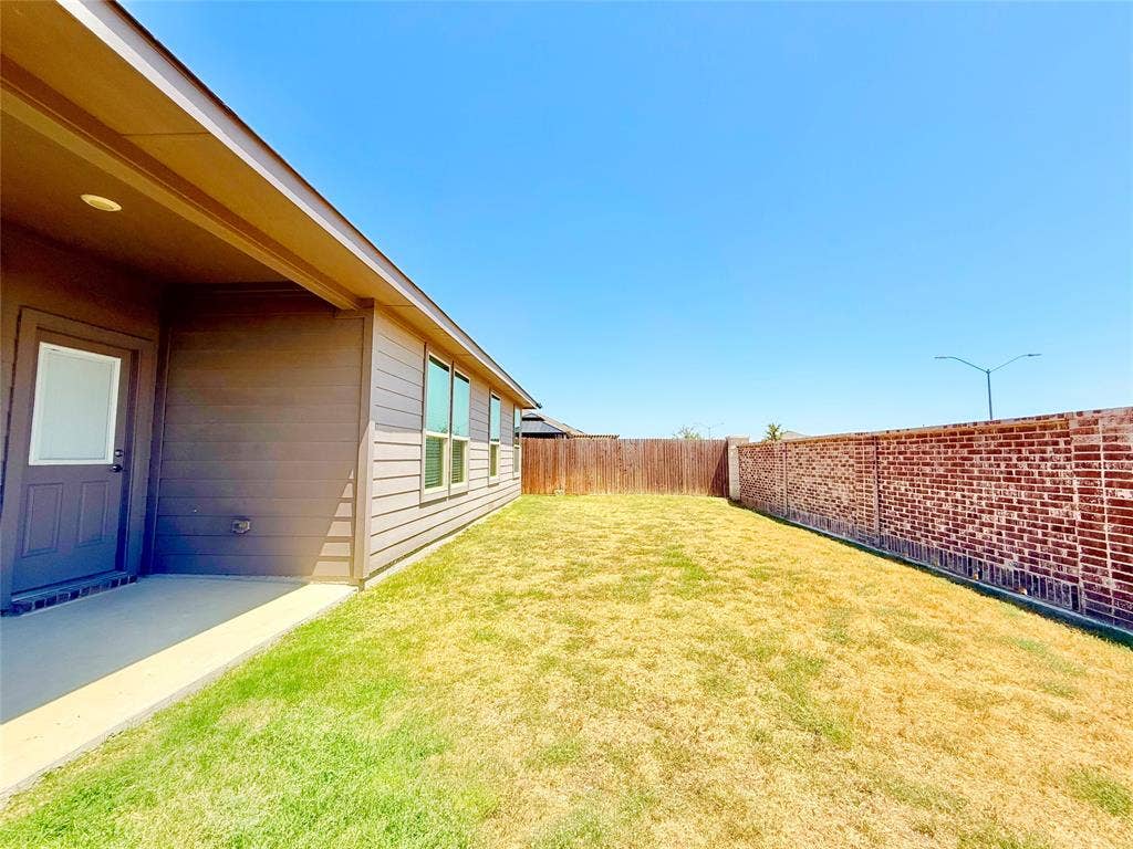 Covered concrete patio, siding exterior, expansive lawn, and partial brick perimeter wall