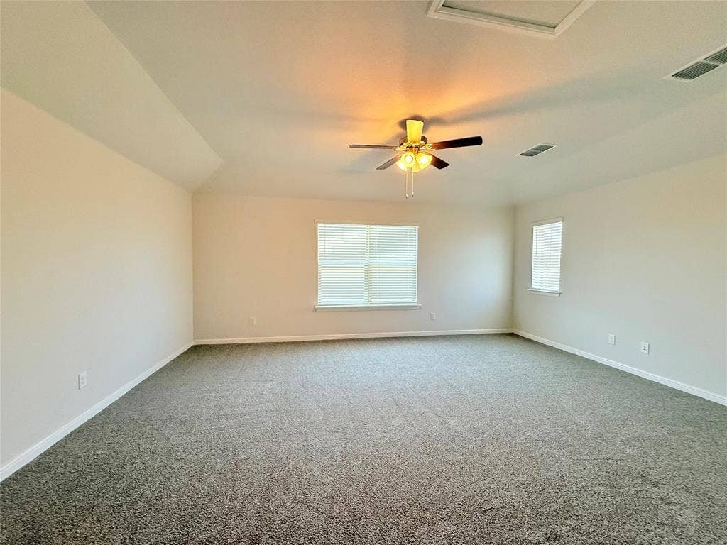 Spacious room featuring neutral carpeting, vaulted ceilings, multi-pane windows with blinds, and a ceiling fan with integrated lighting