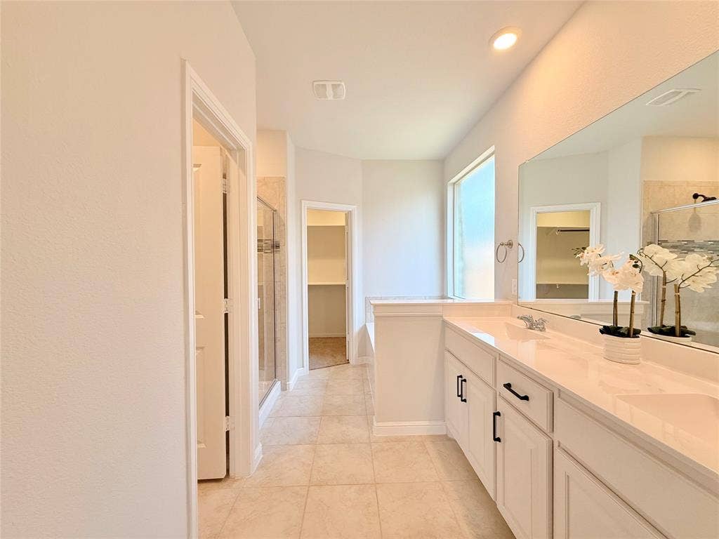 Double vanity with light-toned countertops, white shaker-style cabinetry featuring matte black hardware, tile flooring, and a large wall-mounted mirror