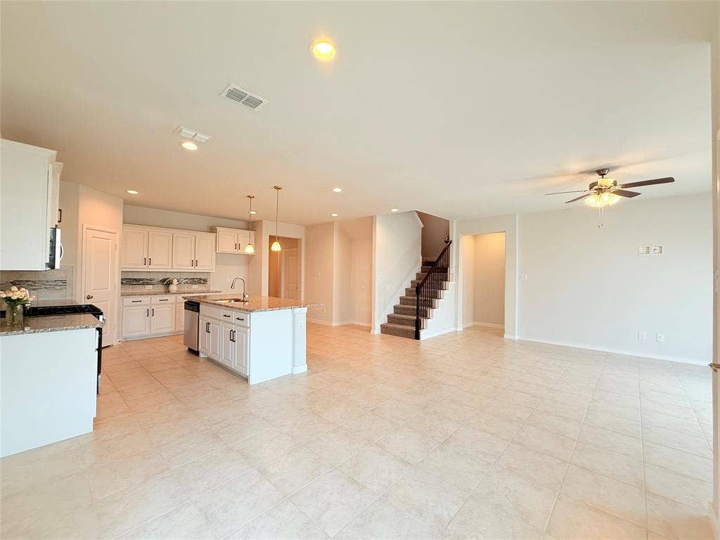 Kitchen featuring white cabinetry, an island with stone-composite countertops, tile flooring, recessed lighting, and a staircase with a black handrail