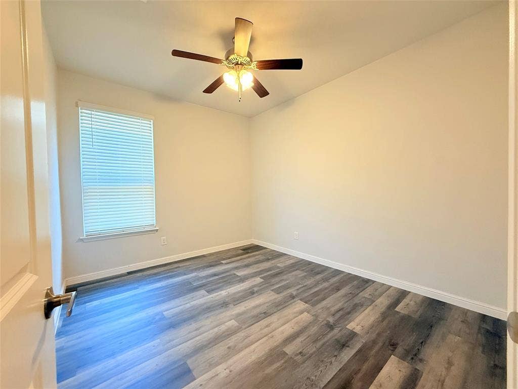 Room featuring wood-finish flooring, a ceiling fan with integrated lighting, and a window with blinds