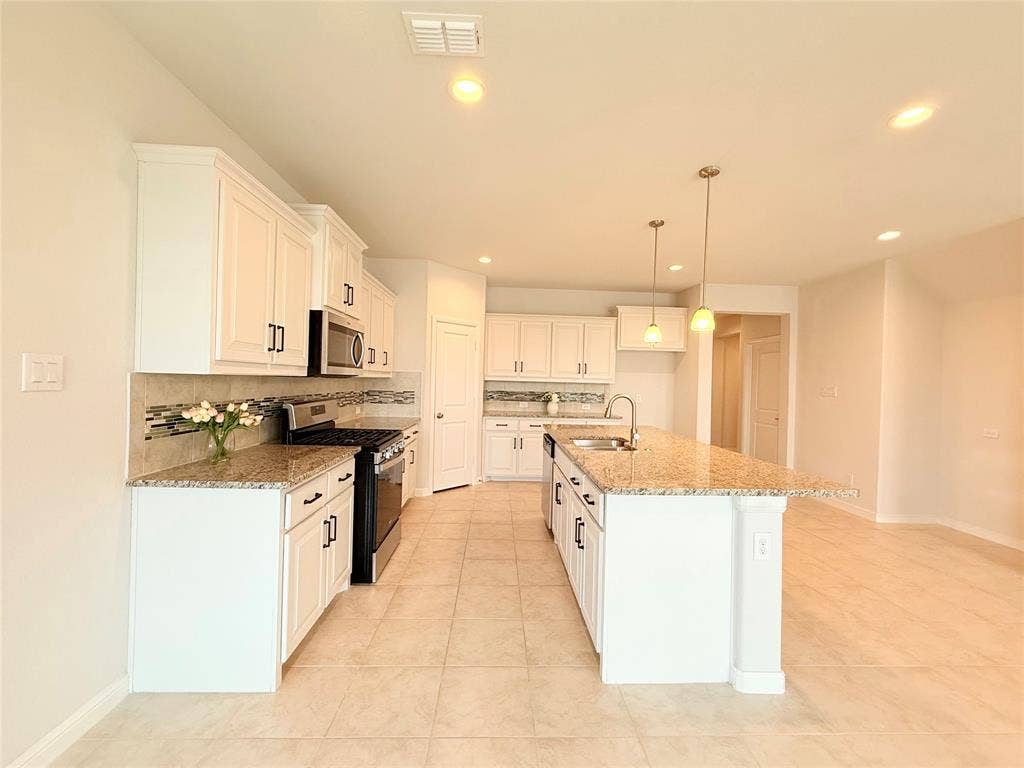 Kitchen featuring white cabinetry, stone-finish countertops, tile backsplash, kitchen island with built-in sink, and tile flooring