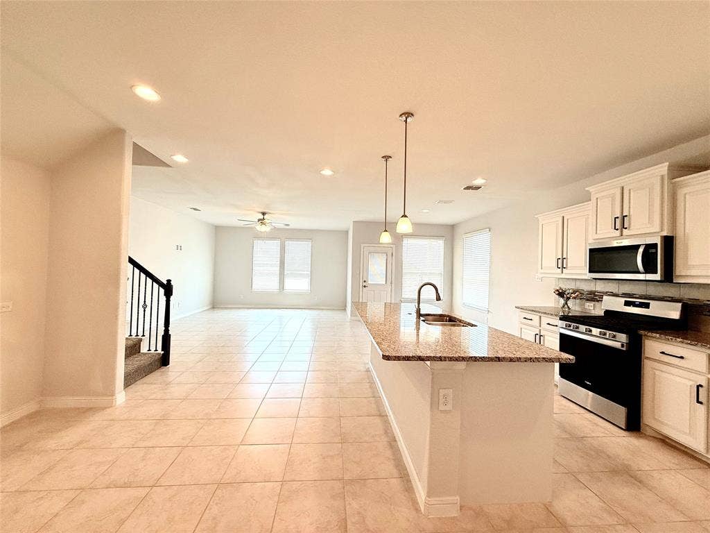 Kitchen featuring white cabinetry, stone-surface countertops, center island with pendant lighting, and stainless steel appliances, including tiled flooring throughout