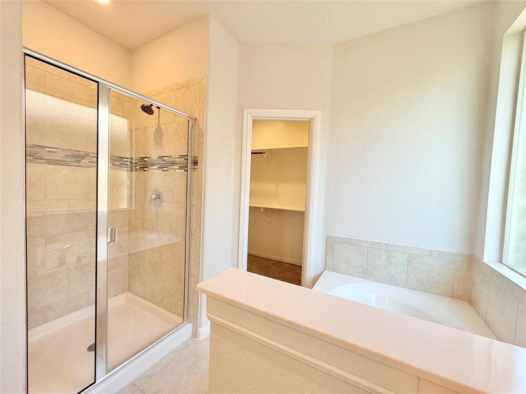 Walk-in shower with glass enclosure and tile surround featuring decorative stone-finish accents, deep soaking tub with tile surround, and built-in closet shelving