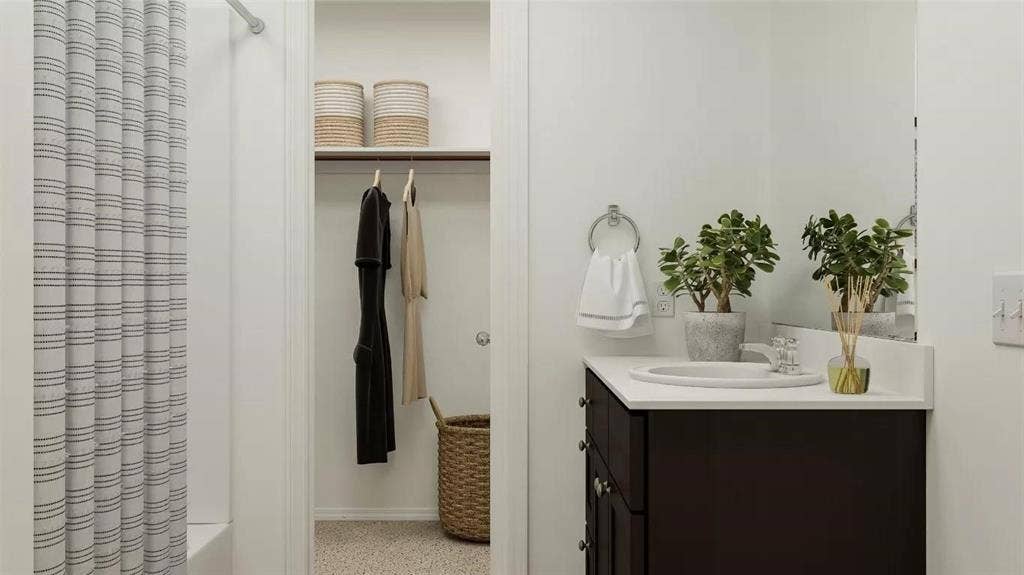 116 Radish Road, Princeton, TX 75407 Bathroom featuring a dark-finish vanity with a white countertop and oval undermount sink, large wall-mounted mirror, brushed-nickel towel ring, and walk-in closet with built-in shelving