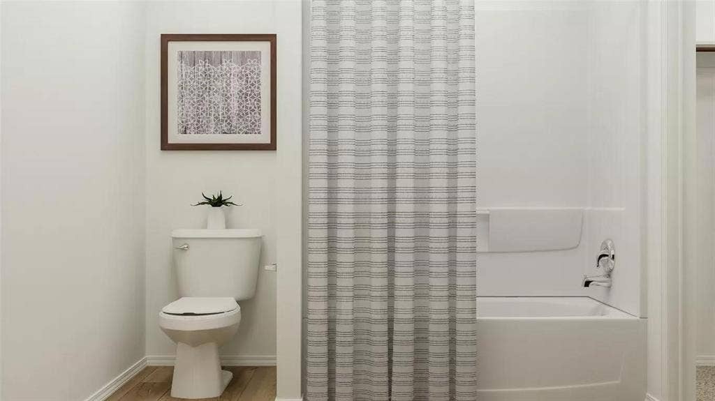 116 Radish Road, Princeton, TX 75407 Full bathroom featuring a white porcelain toilet, a composite tub and shower surround, and polished chrome plumbing fixtures, complemented by wood-finish flooring