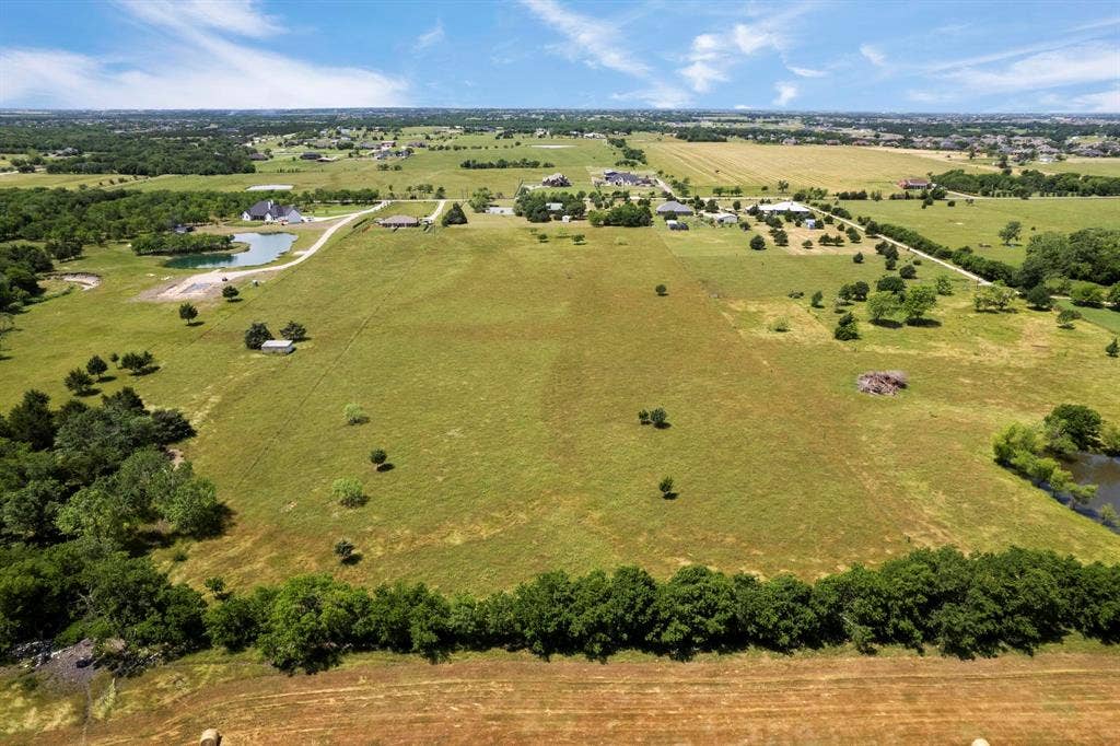 Expansive acreage featuring open pasture, mature tree clusters, and a natural pond