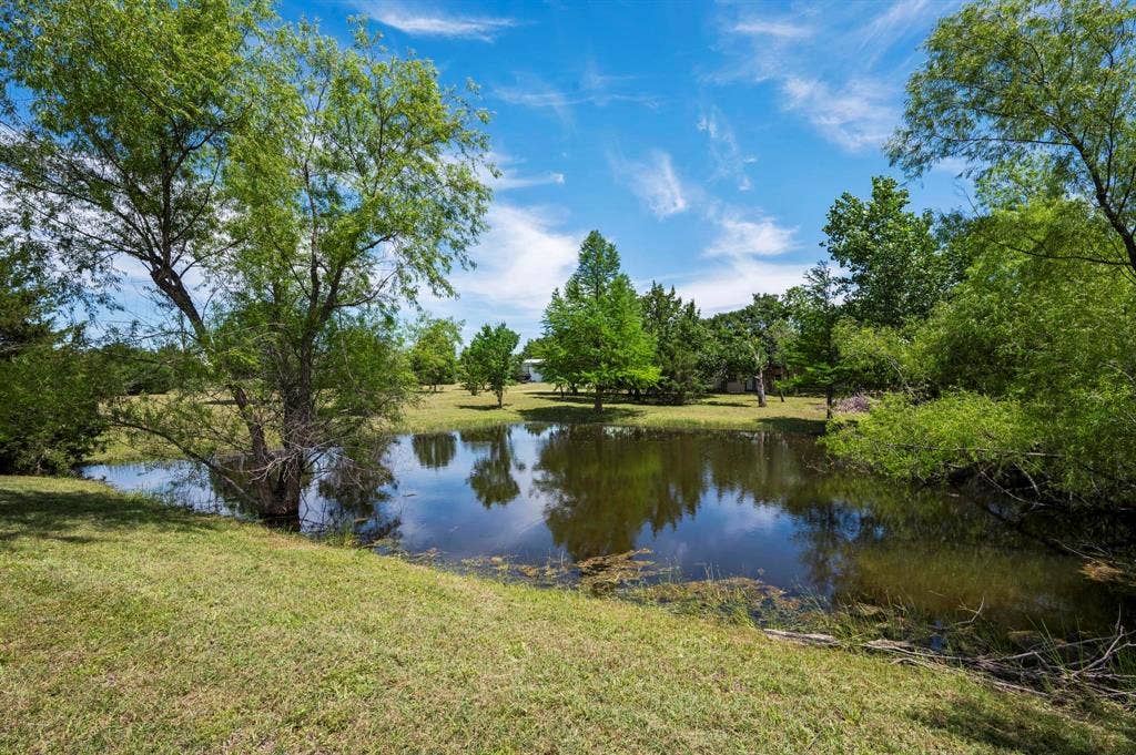 Private pond situated on open acreage featuring mature trees and established landscaping