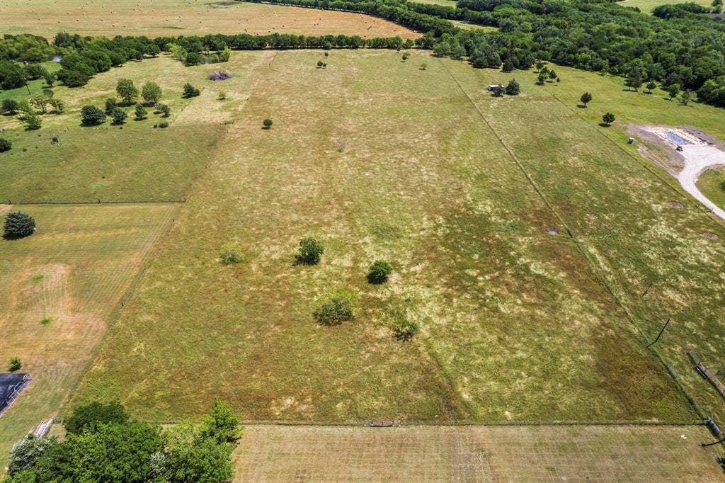 Expansive acreage featuring cleared pasture land, perimeter fencing, scattered mature trees, and gravel access