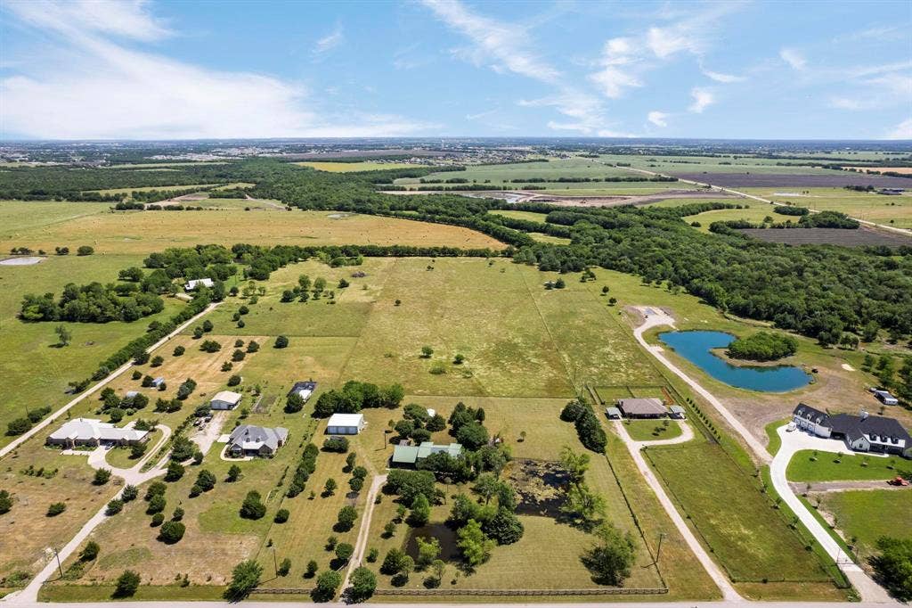 Aerial perspective of expansive acreage featuring fenced pastureland, multiple residential structures, scattered mature trees, and private ponds