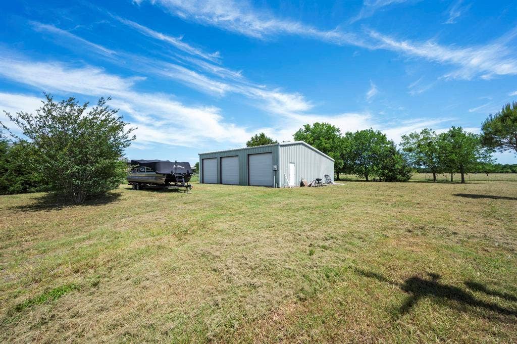 Detached metal outbuilding featuring three roll-up garage doors, situated on expansive grounds