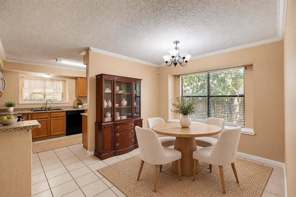 Kitchen and dining area featuring light-tone cabinetry, stone-finish countertops, ceramic tile flooring, crown molding, and a multi-bulb chandelier