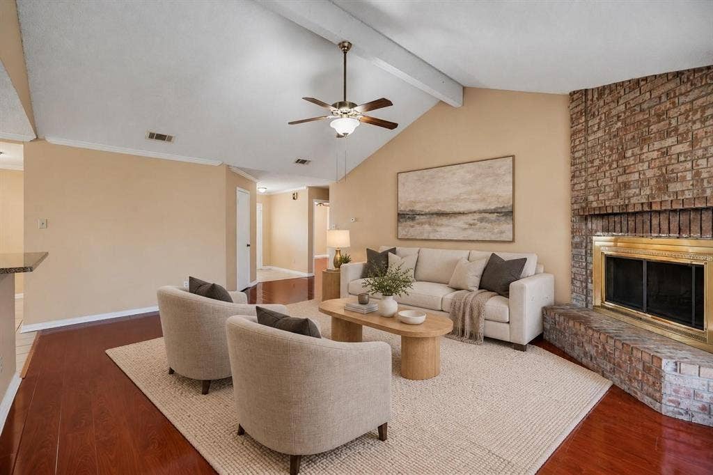 Living area featuring a vaulted ceiling with exposed beam, wood-finish flooring, and a floor-to-ceiling brick fireplace with a metal surround