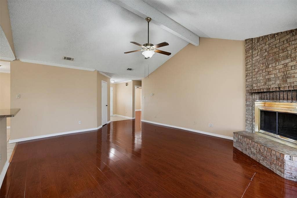 Vaulted ceiling with exposed beam, wood-finish flooring, and brick fireplace with a metallic finish surround