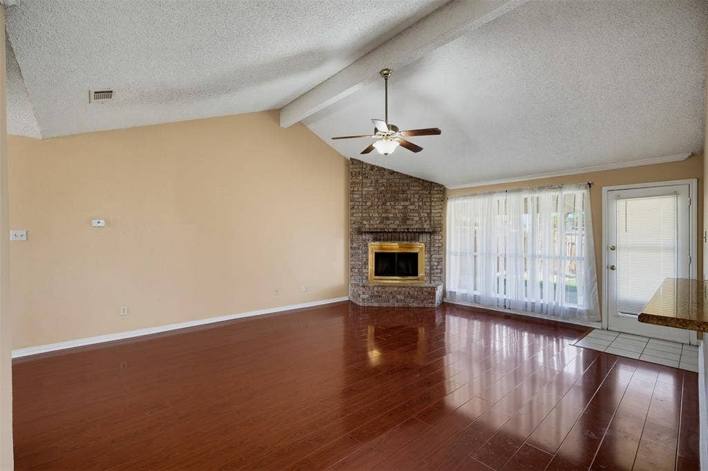 Living area featuring vaulted ceilings with exposed beams, wood-finish flooring, and a stone-clad corner fireplace with a metal surround