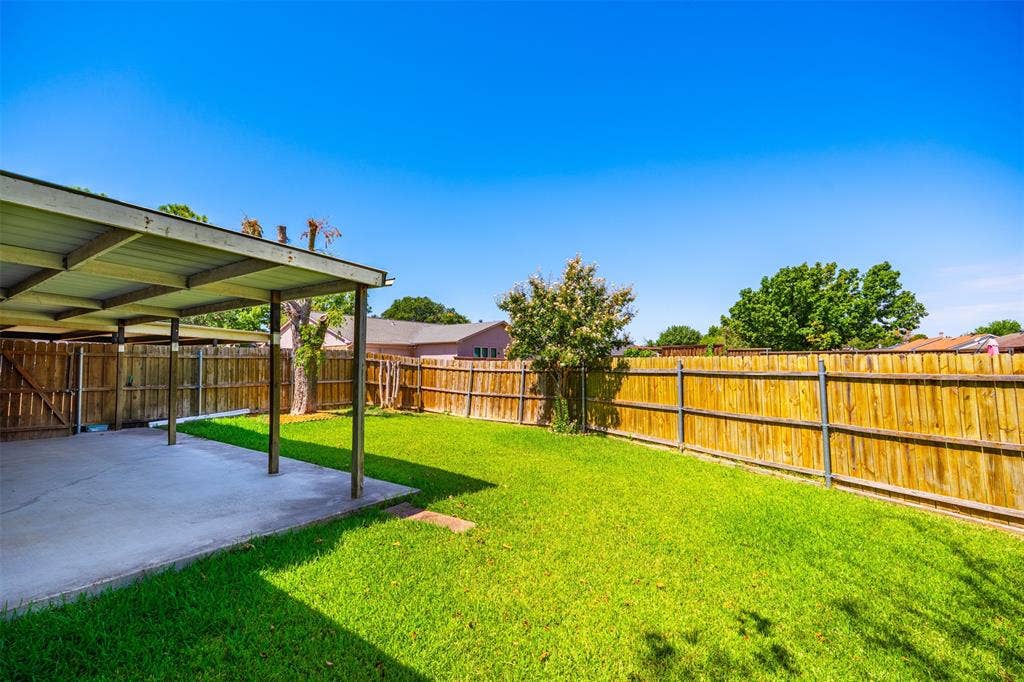 Backyard featuring a concrete-floored covered patio, wood privacy fencing, and a grass lawn
