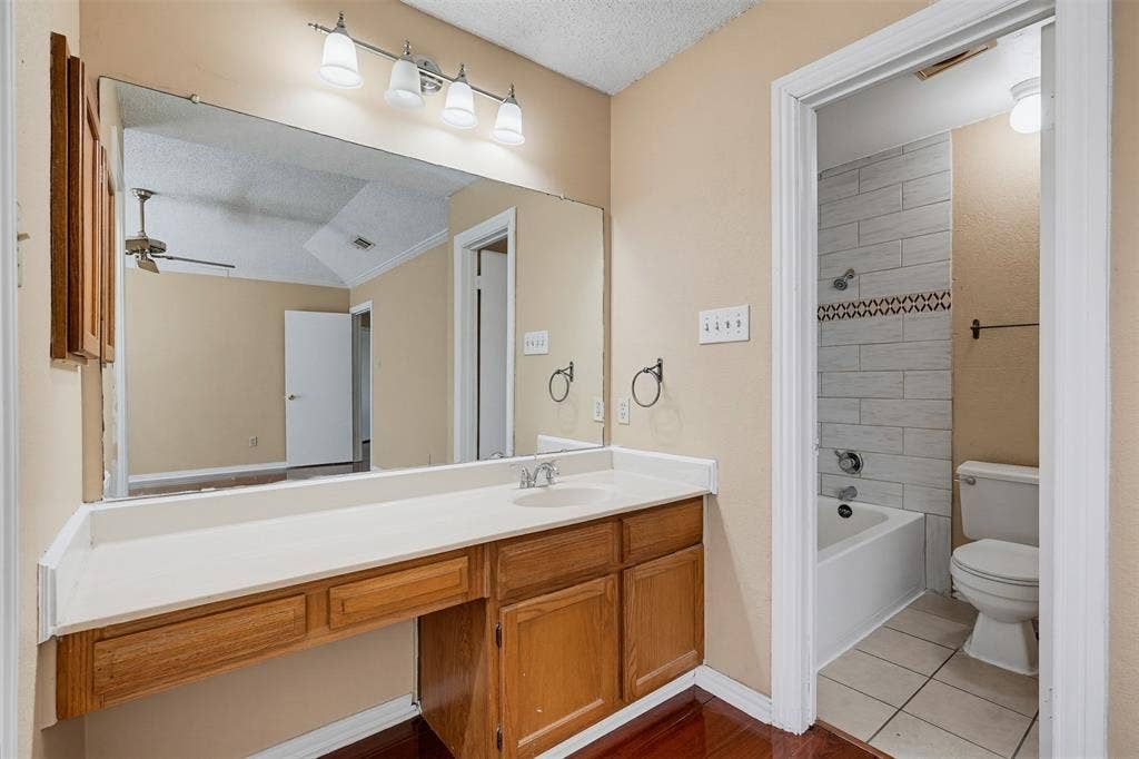 Bathroom featuring a vanity with wood-finish cabinetry, a white countertop with an integrated basin, a large wall-mounted mirror, four-light vanity fixture, and a tiled shower-tub combination