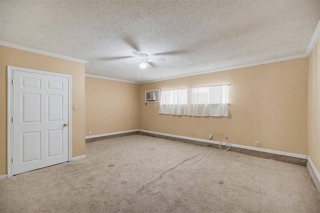 Interior space featuring neutral wall tones, wall-to-wall carpeting, a multi-panel door, a ceiling fan with light fixture, and a window unit air conditioner