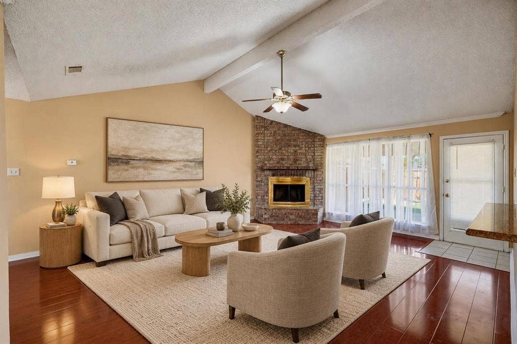 Vaulted ceiling with exposed beam, corner masonry fireplace with hearth, and dark wood-finish flooring